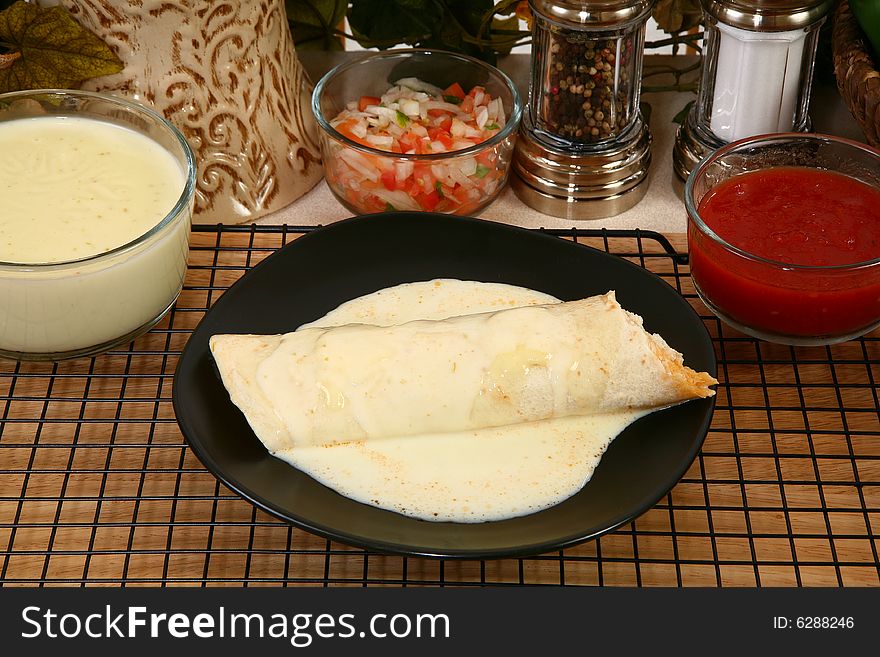 Chicken burrito in plate covered in cheese dip in kitchen or restaurant.