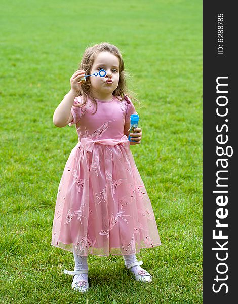 Little girl in pink dress is blowing bubbles on green grass. Little girl in pink dress is blowing bubbles on green grass