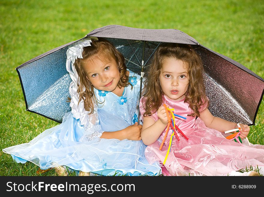 Two little girls are sitting under umbrella on green grass. Two little girls are sitting under umbrella on green grass