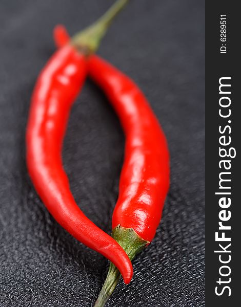 Two red chillies on black leather background