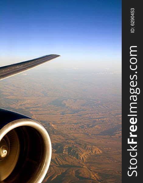 View of a jet engine and wing over mountainous terrain. View of a jet engine and wing over mountainous terrain