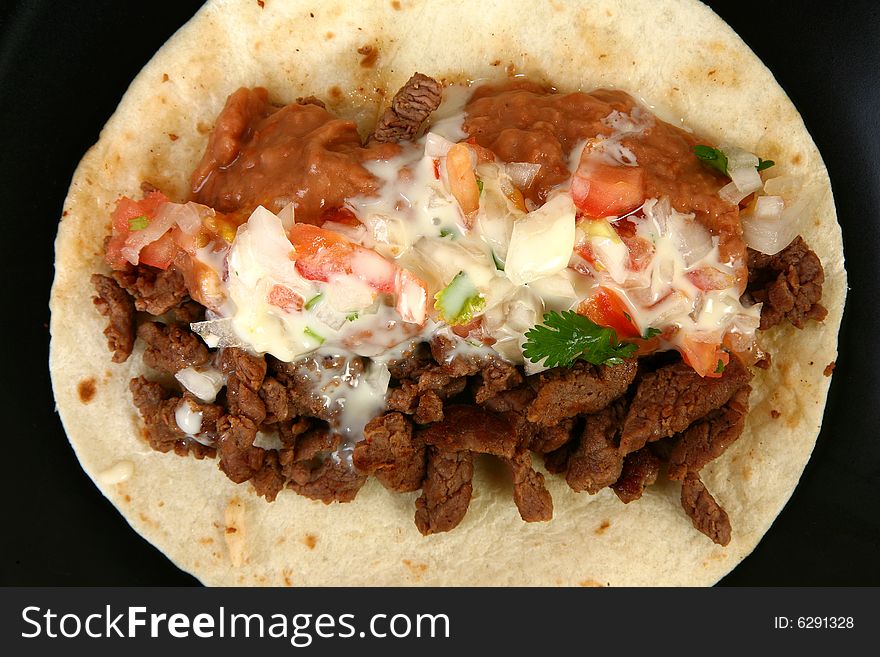 Taco Carne Asada in restaurant or kitchen setting. Beef, beans, Pico de Gallo, cheese dip. Taco Carne Asada in restaurant or kitchen setting. Beef, beans, Pico de Gallo, cheese dip.