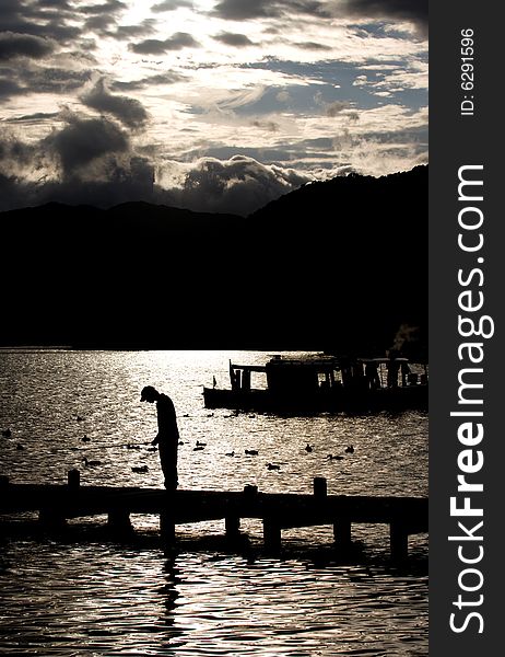 Silhouette of boy fishing from a Jetty on Lake Windermere. Silhouette of boy fishing from a Jetty on Lake Windermere