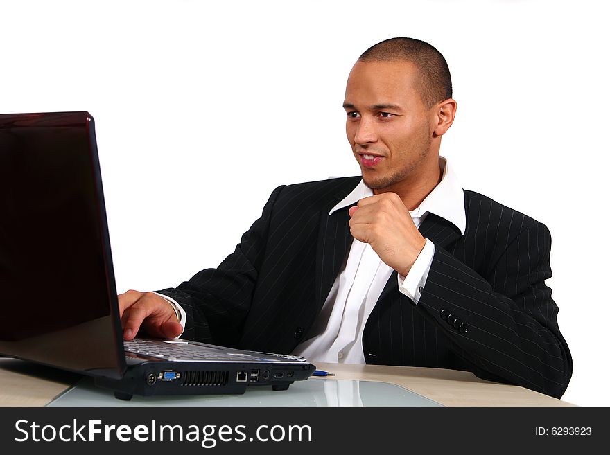 A young businessman sitting by desk at office working on the laptop with a table out of glass and wood. A young businessman sitting by desk at office working on the laptop with a table out of glass and wood.