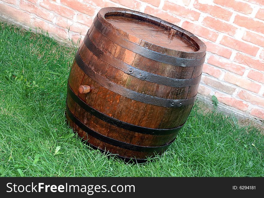 Old wooden wine brown barrel over grass and brick wall. Old wooden wine brown barrel over grass and brick wall