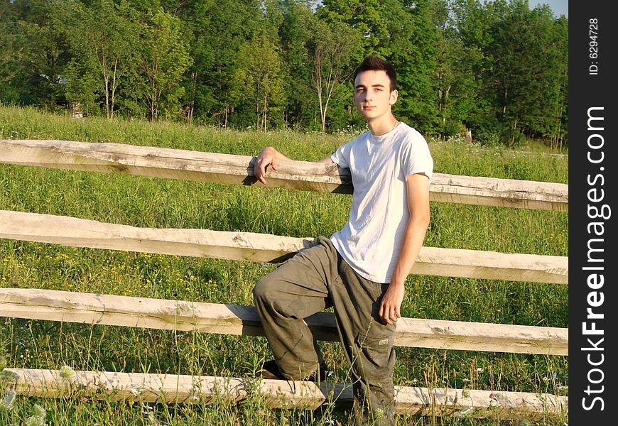 Young country boy leaning against a fence in a field. Young country boy leaning against a fence in a field.