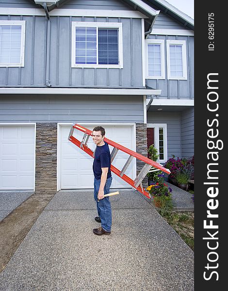 Smiling man standing in front of house holding ladder and hammer. Vertically framed photo. Smiling man standing in front of house holding ladder and hammer. Vertically framed photo.