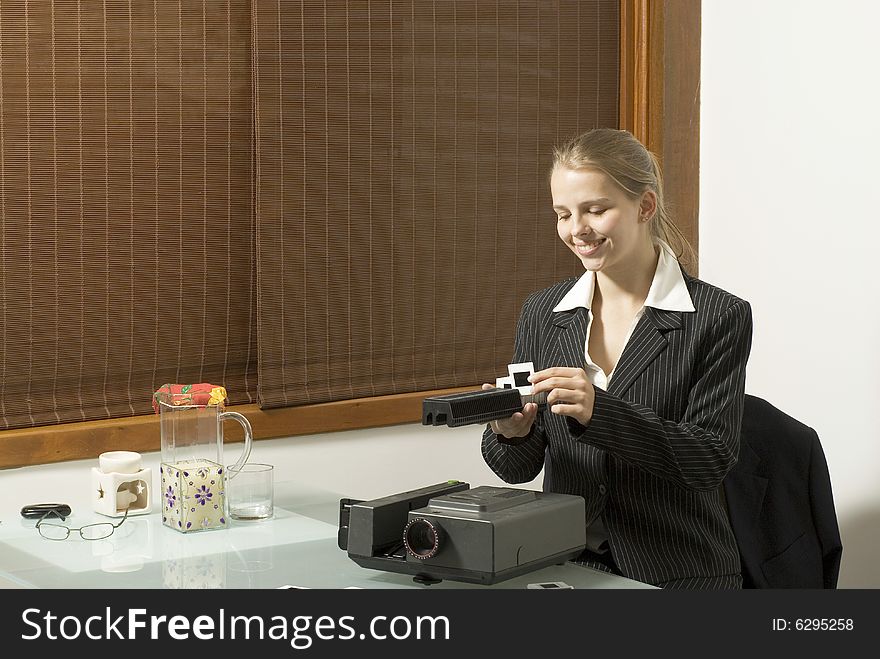 Woman smiling as she places slides in  a slide show projector. There is a pitcher of lemonade and a candle nearby. Horizontally framed photo. Woman smiling as she places slides in  a slide show projector. There is a pitcher of lemonade and a candle nearby. Horizontally framed photo.