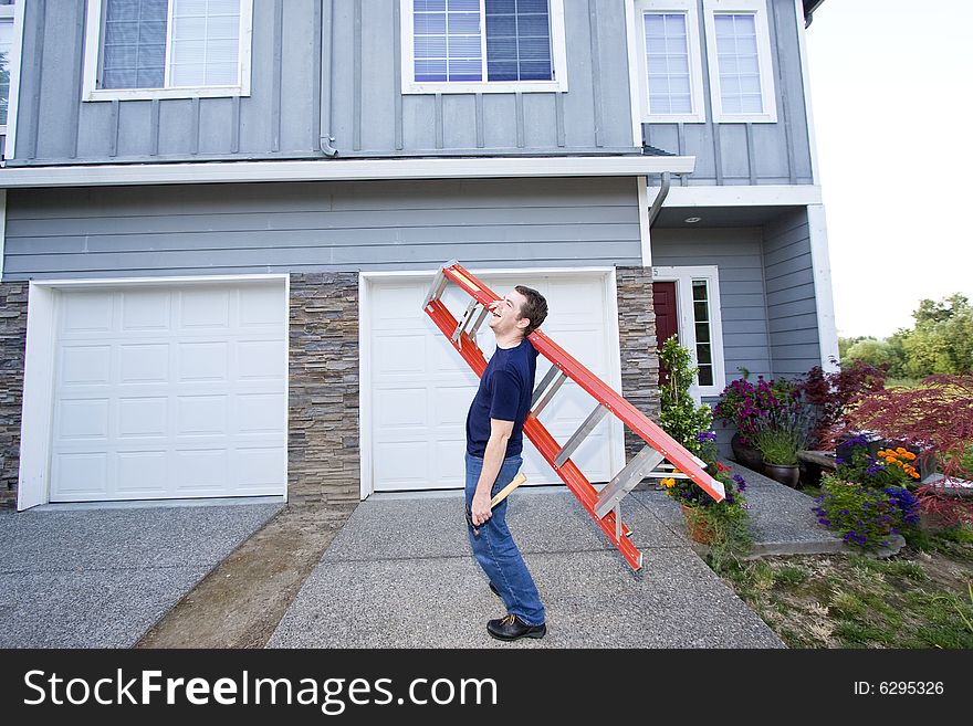 Laughing man standing in front of house holding ladder and hammer. Horizontally framed photo. Laughing man standing in front of house holding ladder and hammer. Horizontally framed photo.