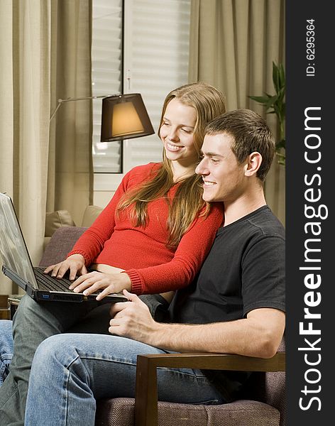 Young smiling, couple at home working on a laptop computer. Vertically framed photo. Young smiling, couple at home working on a laptop computer. Vertically framed photo.