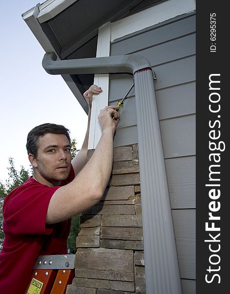 Man standing on a ladder fixing a house with a screwdriver. Vertically framed photo. Man standing on a ladder fixing a house with a screwdriver. Vertically framed photo.