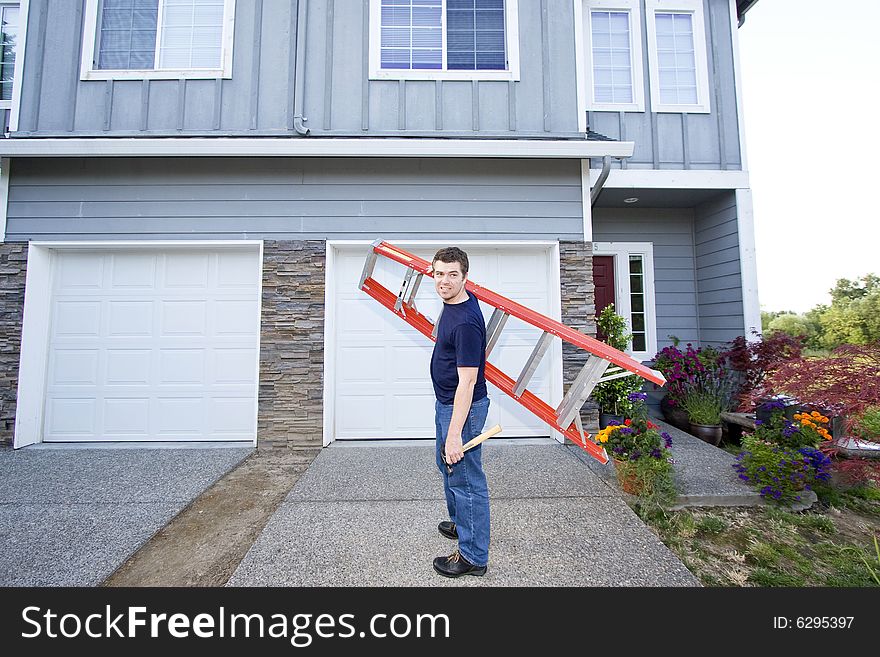 Smiling man standing in front of house holding ladder and hammer. Horizontally framed photo. Smiling man standing in front of house holding ladder and hammer. Horizontally framed photo.