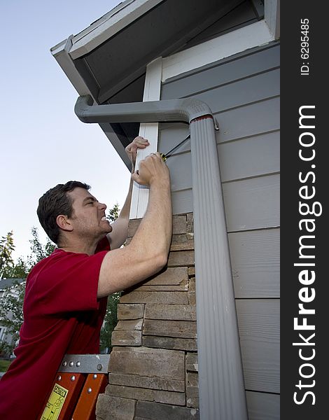 Grimacing man standing on a ladder fixing a house with a screwdriver. Vertically framed photo. Grimacing man standing on a ladder fixing a house with a screwdriver. Vertically framed photo.