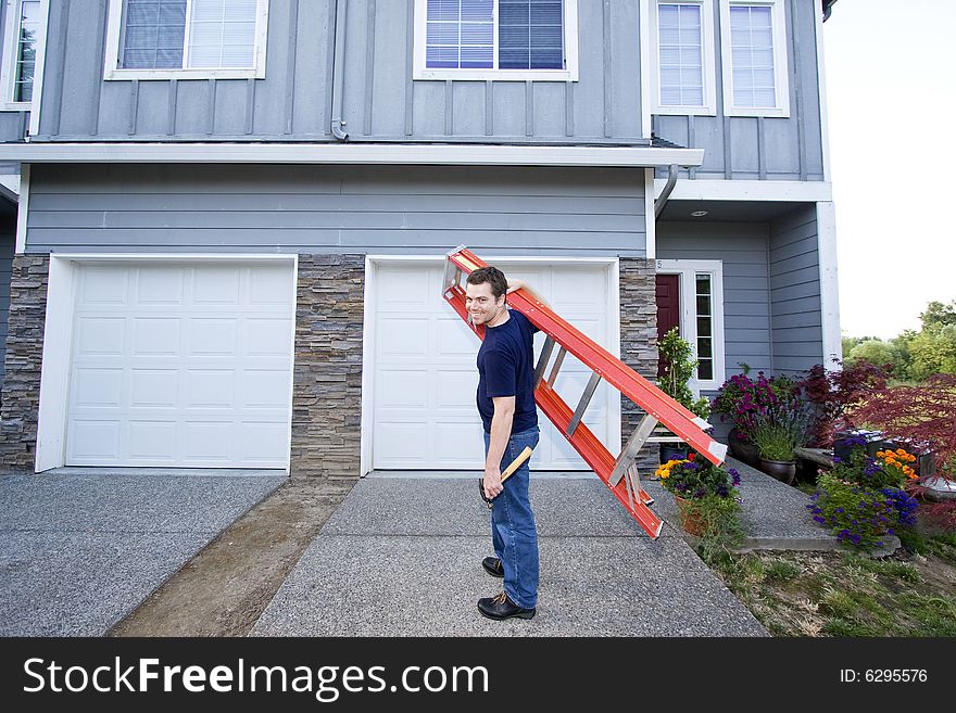 Smiling man standing in front of house holding ladder and hammer. Horizontally framed photo. Smiling man standing in front of house holding ladder and hammer. Horizontally framed photo.