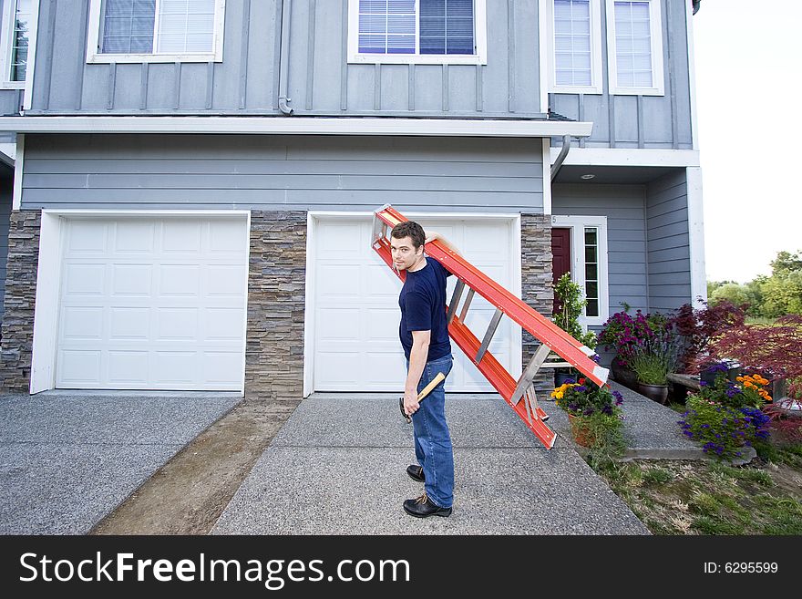 Man standing in front of house holding ladder and hammer. Horizontally framed photo. Man standing in front of house holding ladder and hammer. Horizontally framed photo.