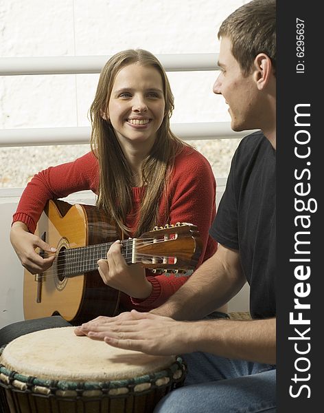 Woman playing guitar as she looks at the man next to her on the drums. Vertically framed photo. Woman playing guitar as she looks at the man next to her on the drums. Vertically framed photo.