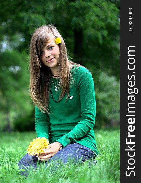 Photo presents a teenager on a grass holding a yellow flower. Photo presents a teenager on a grass holding a yellow flower