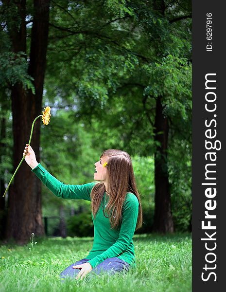 Photo presents a teenager on a grass holding a yellow flower. Photo presents a teenager on a grass holding a yellow flower