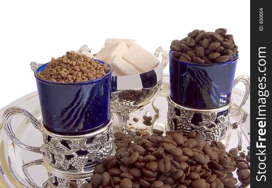Two cups, refined sugar, instant coffee and coffee beans. Two cups, refined sugar, instant coffee and coffee beans