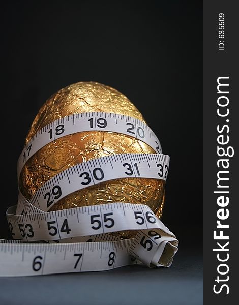 Image of a gold easter egg with a tape measure wrapped around it, conceptual dieting. Image of a gold easter egg with a tape measure wrapped around it, conceptual dieting