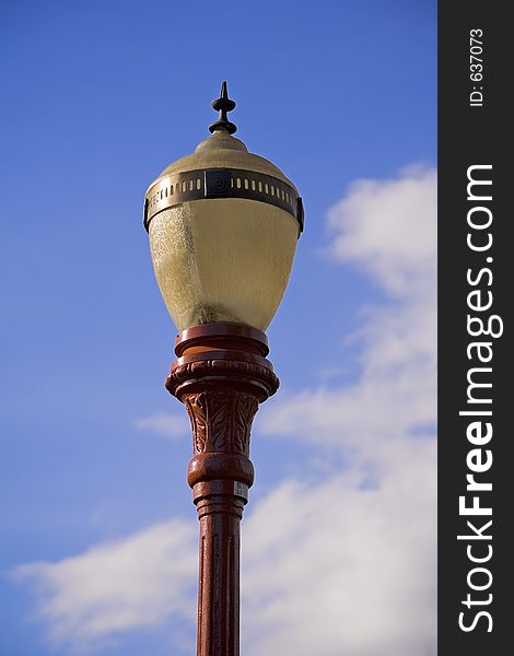 Old lampost on a blue sky background with some white clouds.