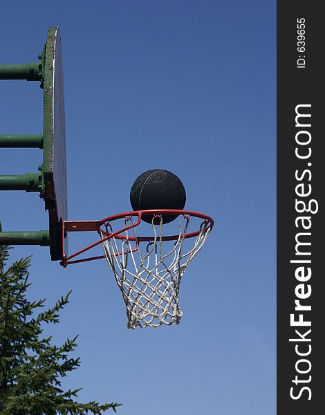 A black basketball rides the basketball rim. A black basketball rides the basketball rim