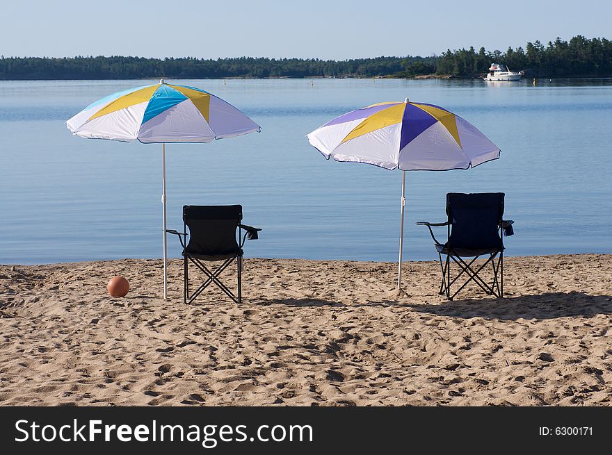 Two beach umbrellas and chairs in the sand at the lake. Two beach umbrellas and chairs in the sand at the lake