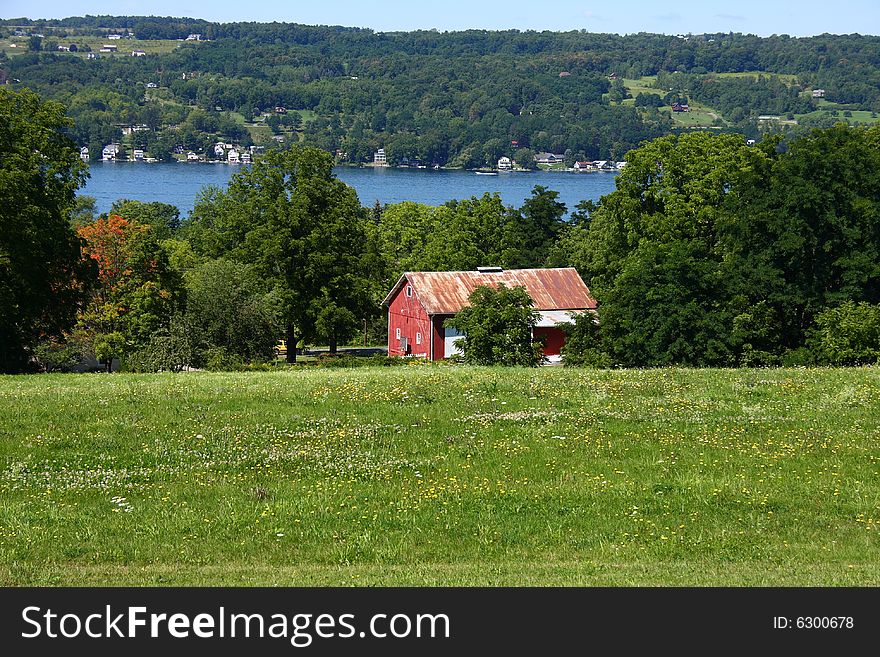 A small red barn or farmhouse in a field near a lake