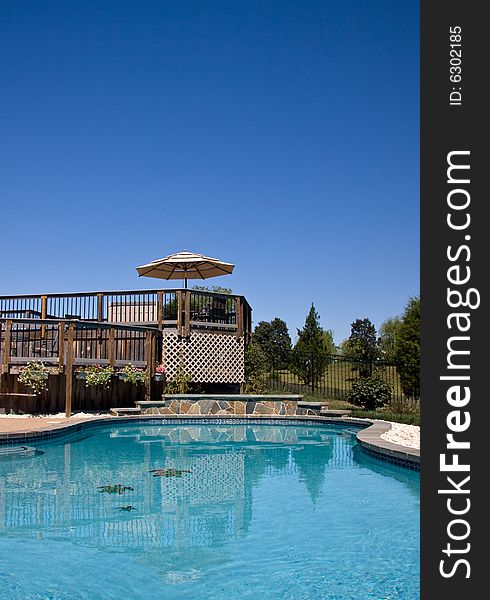 Blue swimming pool looking towards a wooden deck with umbrella and seats. Blue swimming pool looking towards a wooden deck with umbrella and seats