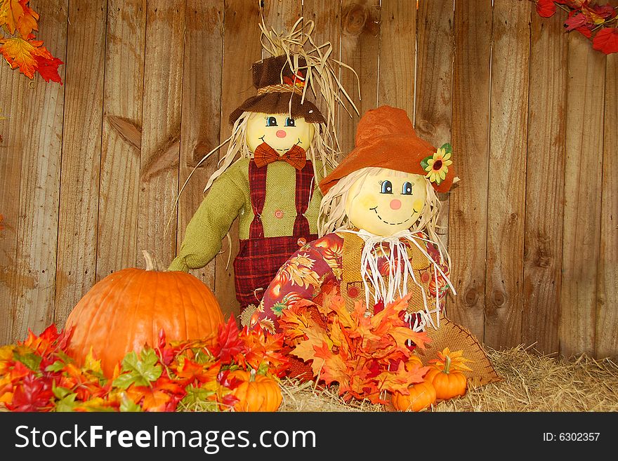 Happy scarecrows display, with pumpkin and fall leaves on straw bale. Room for text. Happy scarecrows display, with pumpkin and fall leaves on straw bale. Room for text.