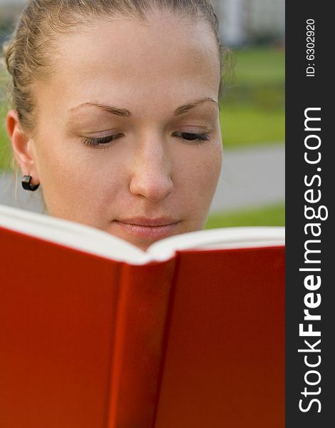 Outdoor portrait of pretty woman with red book