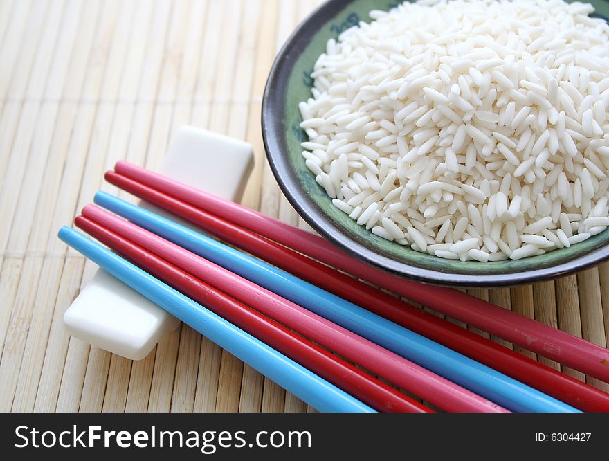 Some asian rice in a bowl and colorful chopsticks
