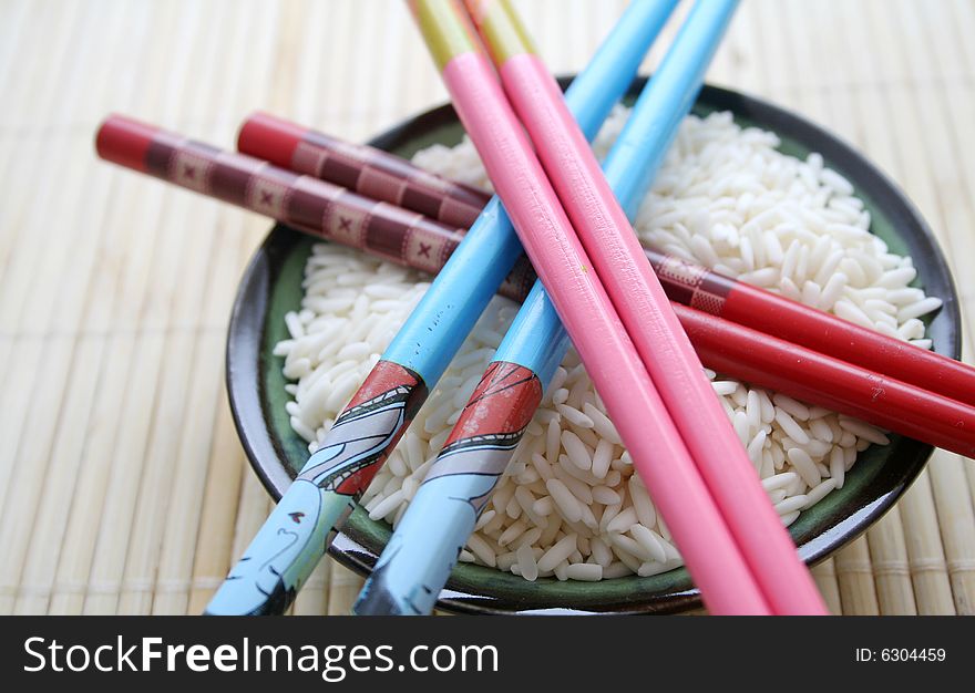 Some asian rice in a bowl and colorful chopsticks