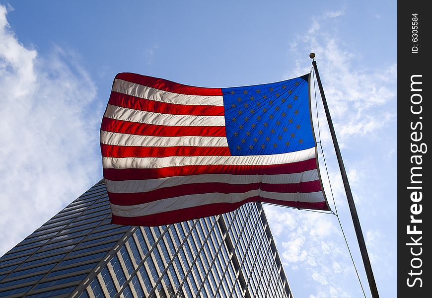 American flag waving against a skyscraper and a blue sky.