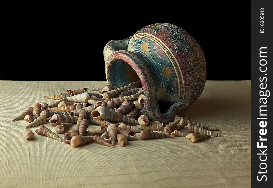 Hand painted clay pot on side dumping shells on textured cloth and black background. Hand painted clay pot on side dumping shells on textured cloth and black background