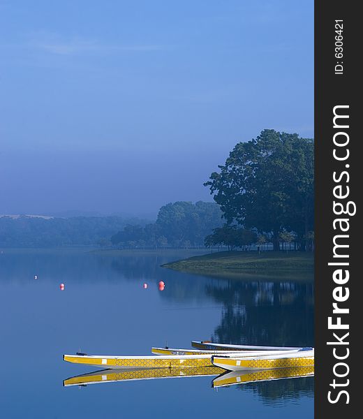 Bathing in the morning sunlight, with clear reflection in water, four sporting boats park quietly in a foggy lake. Red ball marked racing lanes in the background. Bathing in the morning sunlight, with clear reflection in water, four sporting boats park quietly in a foggy lake. Red ball marked racing lanes in the background.