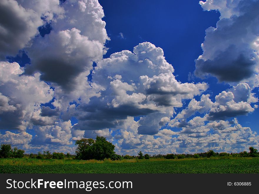 Summer clouds float in a blue sky over an open field in the countryside. Summer clouds float in a blue sky over an open field in the countryside.