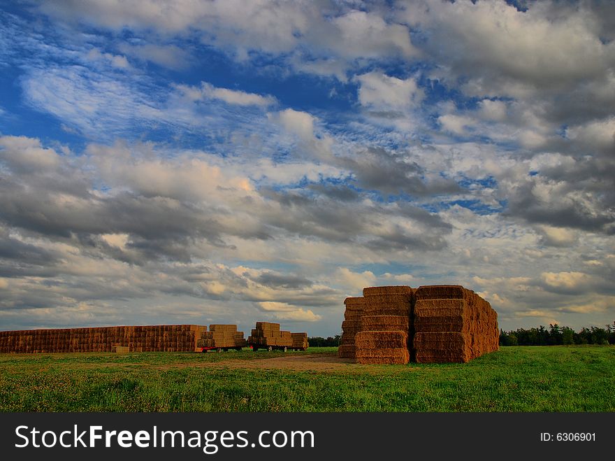 Walls of hay bales under cloudy summer skies. Two more flatbeds are ready to add to the pile. Walls of hay bales under cloudy summer skies. Two more flatbeds are ready to add to the pile.