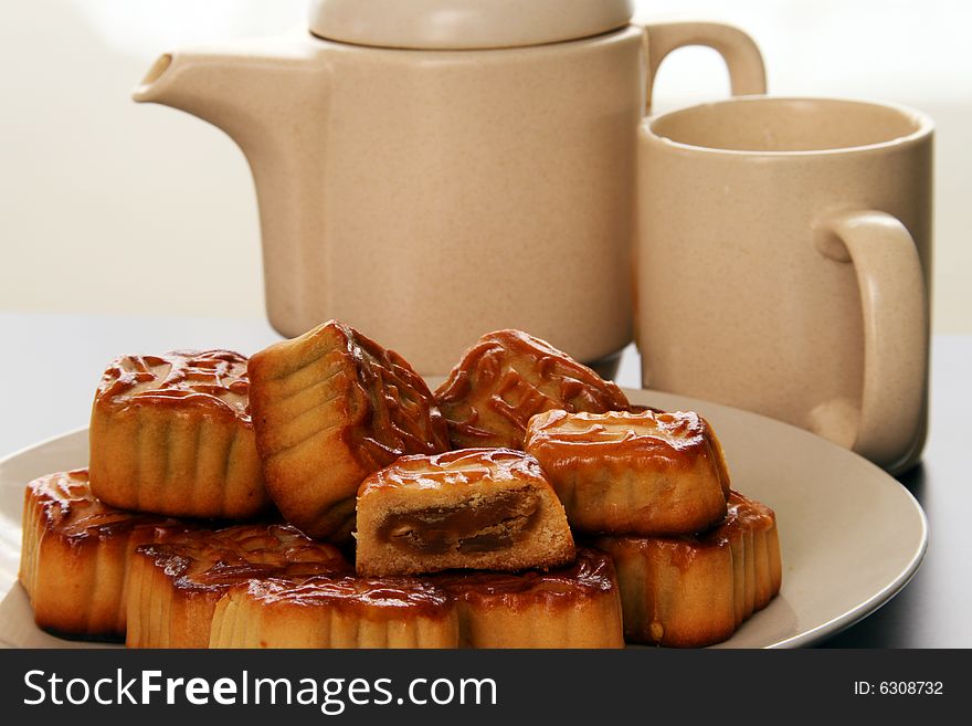 A plate of homemade moon cakes next to a tea pot and cup. A plate of homemade moon cakes next to a tea pot and cup.