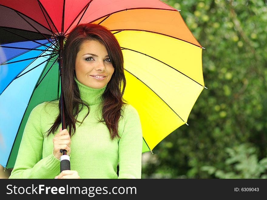 Beautiful woman under colorful umbrella relaxing in park. Beautiful woman under colorful umbrella relaxing in park