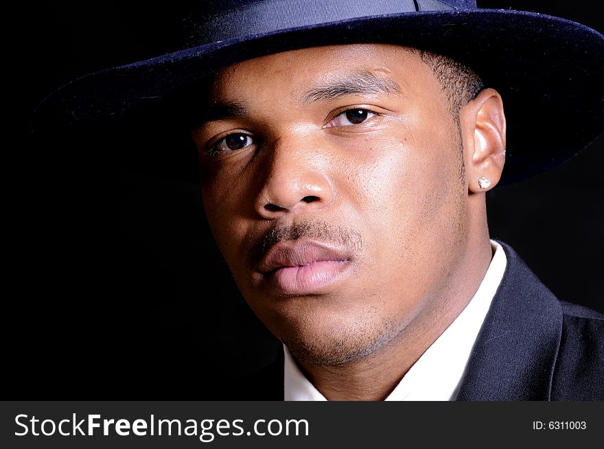 Young African American man in a hat and suit over a black background