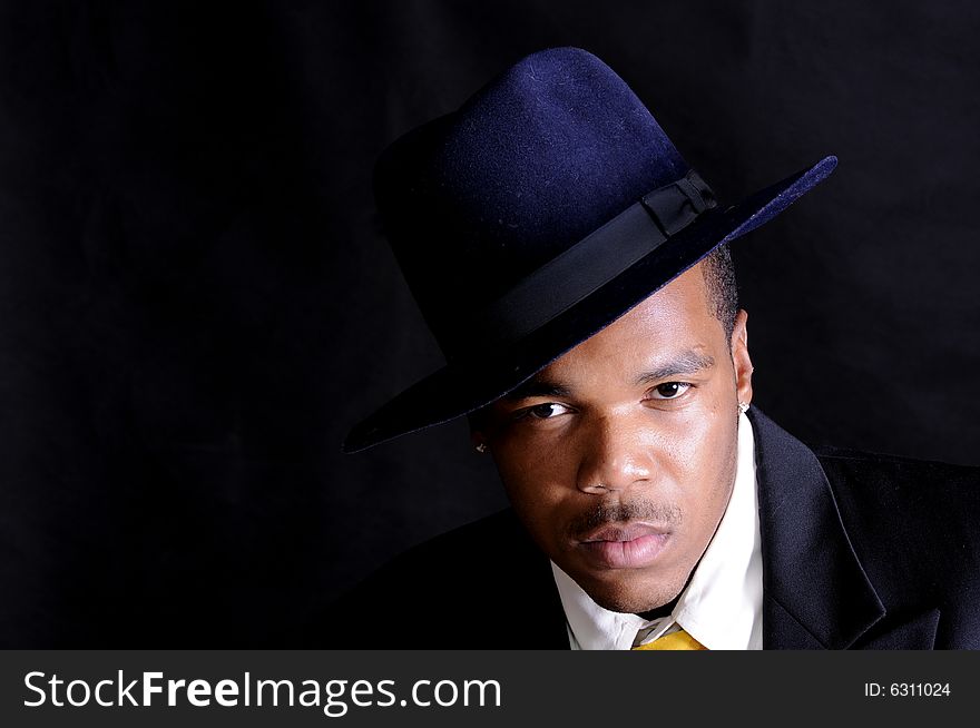 Moody image of a young African American man in a hat and suit over a black background