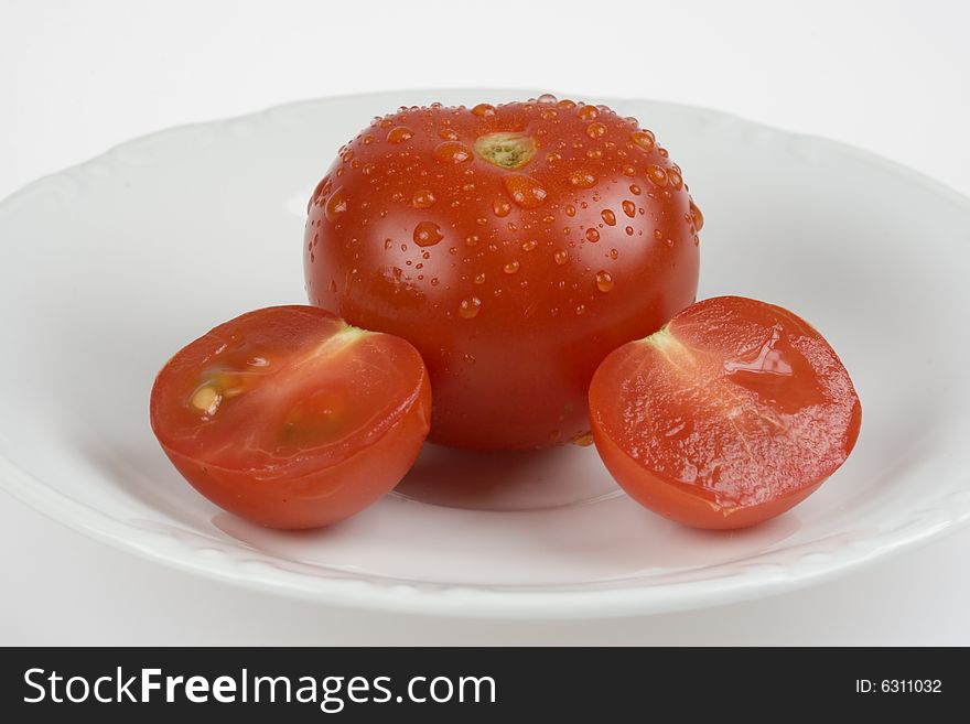 Whole tomato and sliced in two on white plate. Whole tomato and sliced in two on white plate