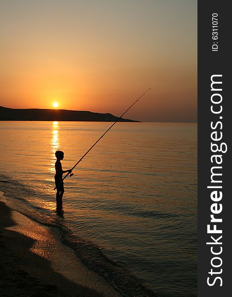 The silhouette of one fisherboy on the Sea of Azov against the background of the  sundown and mountains. The silhouette of one fisherboy on the Sea of Azov against the background of the  sundown and mountains.