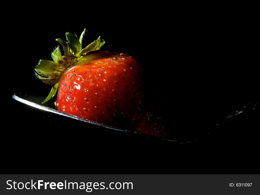 Strawberry sitting on spoon with strong flash from left, and isolated black background. Strawberry sitting on spoon with strong flash from left, and isolated black background
