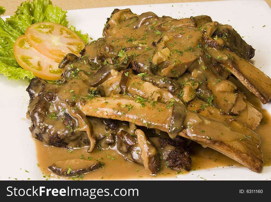 A plate of beef ribs with gravy and mushrooms