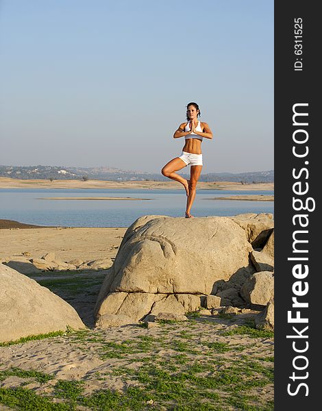 A young woman on top of a rock going yoga at sunset in a white fitness outfit. A young woman on top of a rock going yoga at sunset in a white fitness outfit