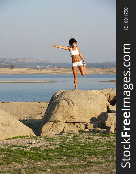 A young woman on top of a rock doing yoga at the lake