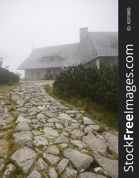 Misty pathway in Polish Tatras on an overcast day, with a tourist hostel detail