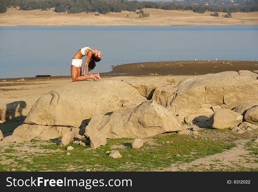 A young woman on top of a rock doing yoga at sunset in a white fitness outfit